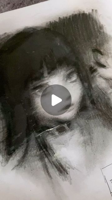 he image shows a closeup of a charcoal drawing depicting a woman's face. the style is expressive and somewhat abstract, with strong use of shading and dark tones. the woman's features are partially obscured by her dark hair, which is rendered with a combination of loose and precise strokes. the overall mood is intense and somewhat mysterious.  a play button is overlaid on the image, suggesting it may be part of a video.  the background is a plain white surface.
