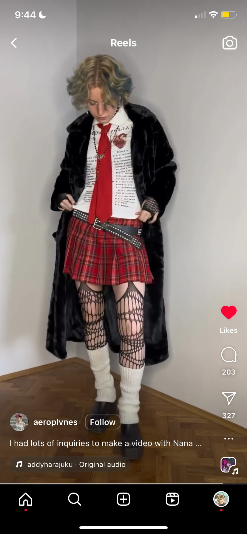 he image shows a young woman wearing a black fur coat, a white graphic shirt, a red and black plaid mini skirt, fishnet tights, white kneehigh socks, and black boots. her hair is styled in short, wavy layers. she's posing in what seems to be a video for social media, with the instagram reels interface visible.  the caption indicates that many people requested a video featuring her and someone named nana.