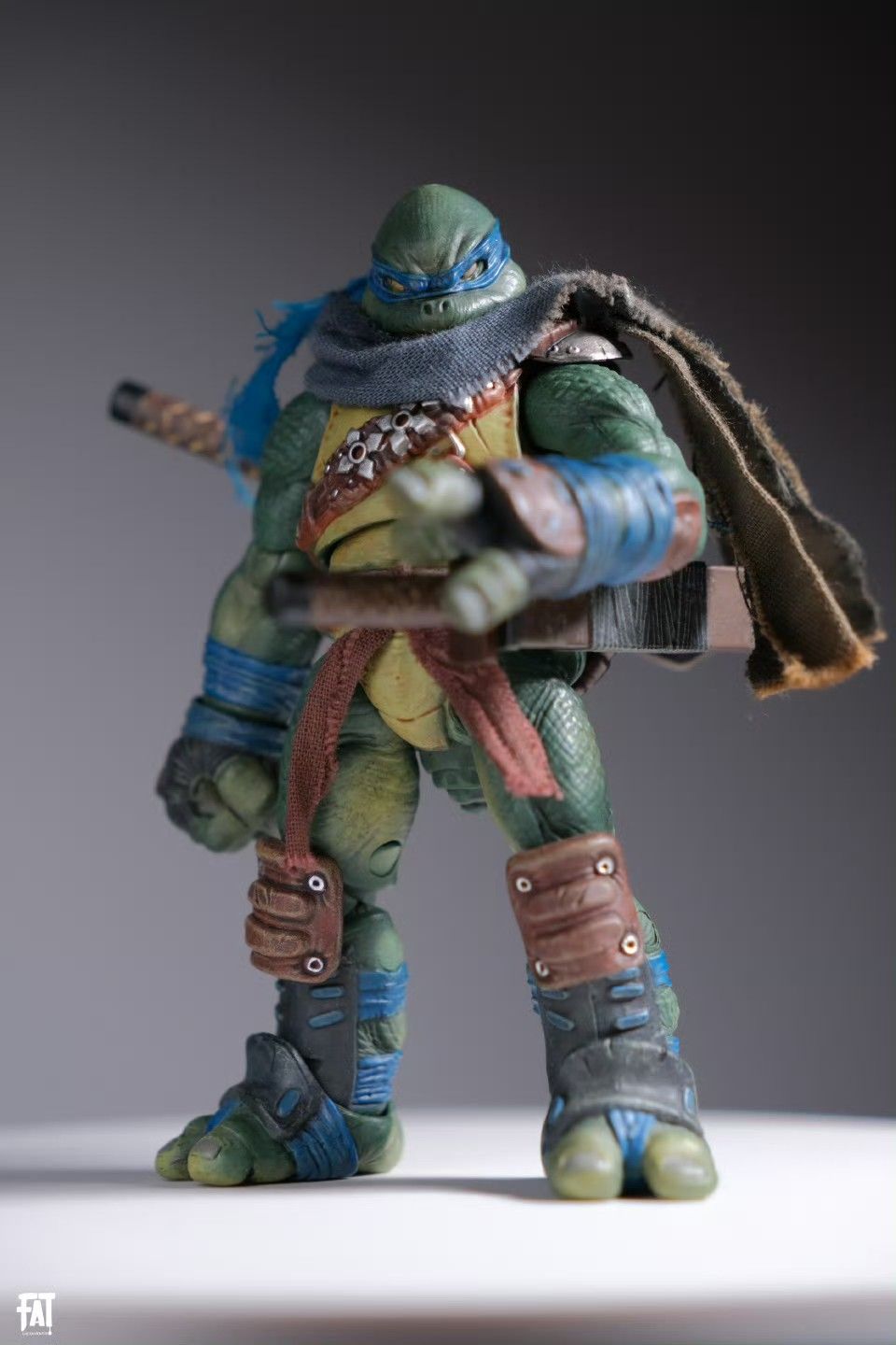 a studio shot of a detailed leonardo action figure from the teenage mutant ninja turtles franchise. the figure is standing and wearing his signature blue bandana and carrying katanas.