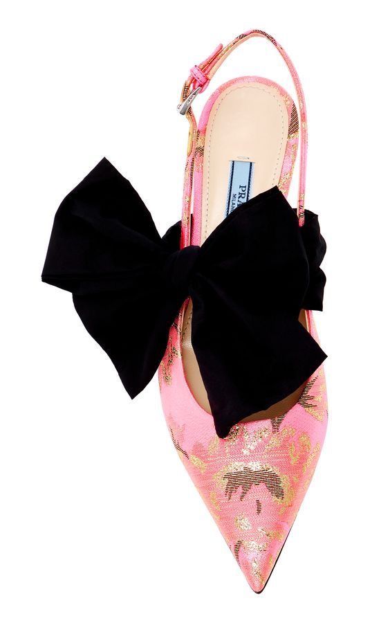 a pink, floralpatterned prada slingback shoe with a large black bow is shown against a white background. the shoe is positioned vertically with the toe pointing down. a large black bow is centered on the shoe and a metal buckle is visible on the slingback strap.