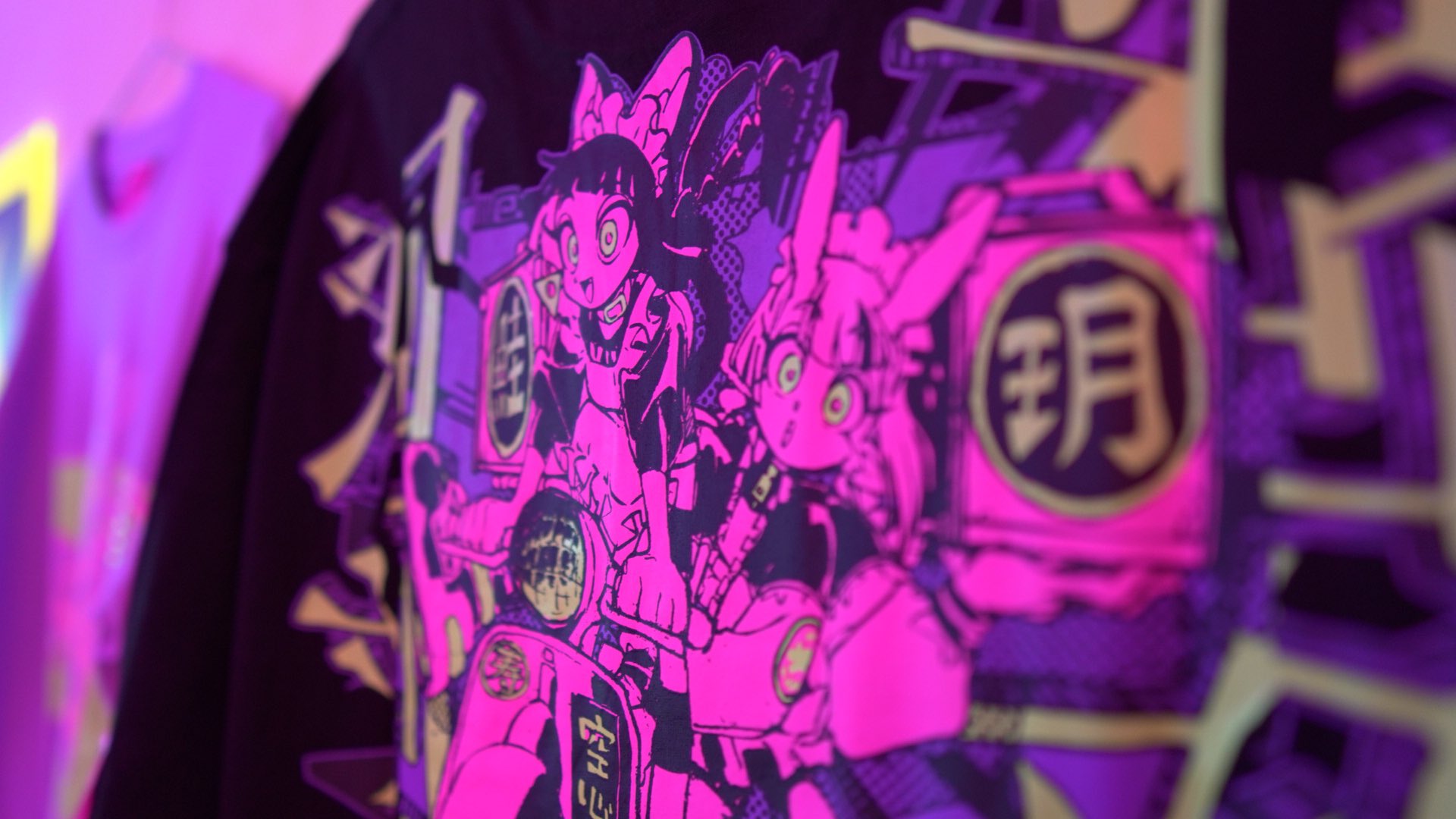 a closeup of a black shirt with two anime girls wearing bunny ear headbands riding on a motorcycle. the illustration is in pink, purple, gold and black. the background is lit with neon lights.