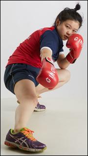 a young woman in boxing attire is captured midmovement, showcasing a powerful boxing stance. she's wearing red and blue sportswear, with the focus on her red boxing gloves. the white background emphasizes her form and the intensity of the action.