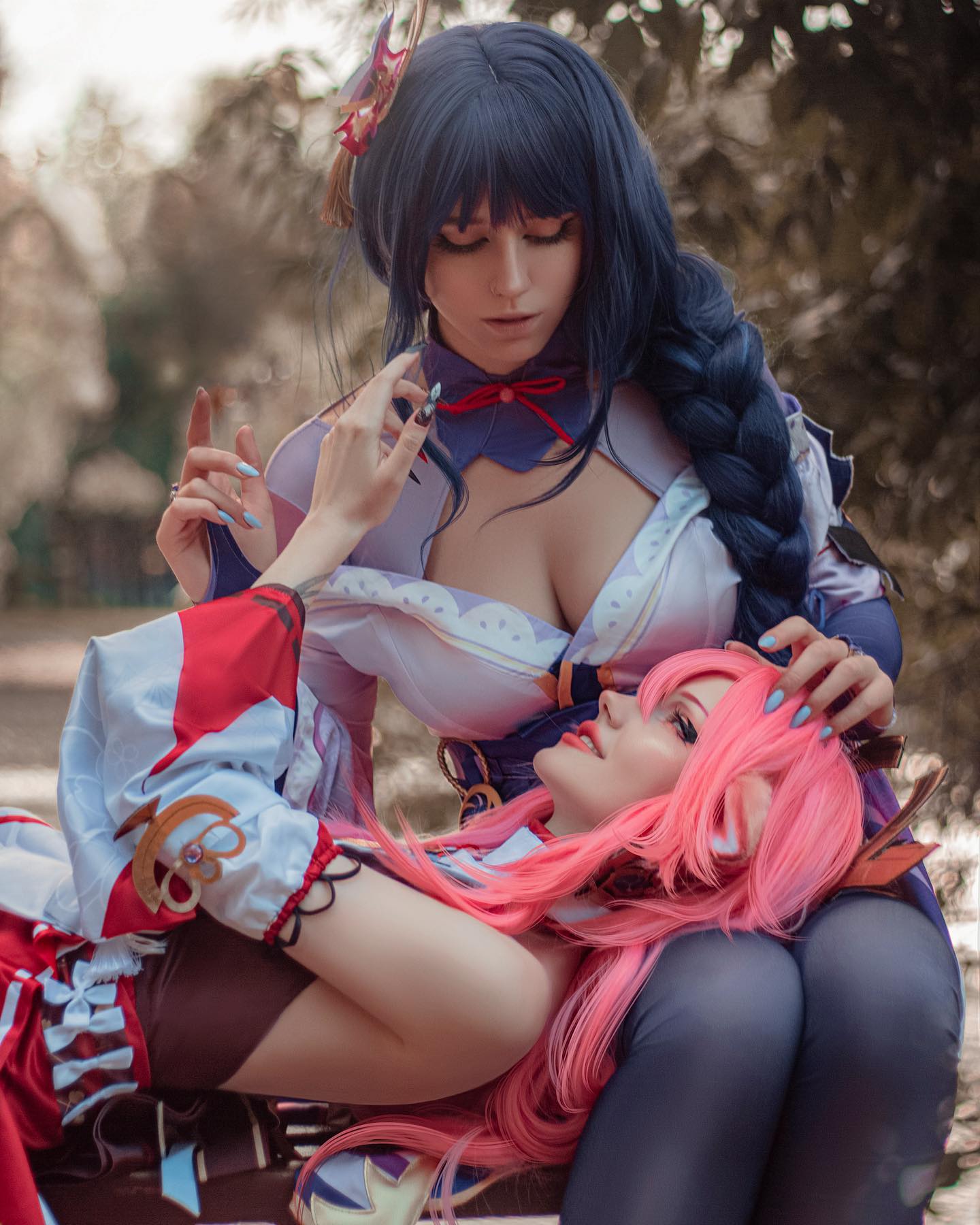 the image is a striking cosplay photoshoot featuring two women dressed as raiden shogun (dark blue hair) and sangonomiya kokomi (pink hair) from the popular video game genshin impact.  raiden shogun is sitting with her arm around kokomi, who is reclining against her.  the cosplayers have meticulously recreated the characters' costumes, wigs, and makeup, capturing the essence of their personalities. the setting is an outdoor parklike area with blurred greenery in the background, providing a soft and natural contrast to the vibrant costumes. the overall atmosphere is one of intimacy and affection between the two characters.