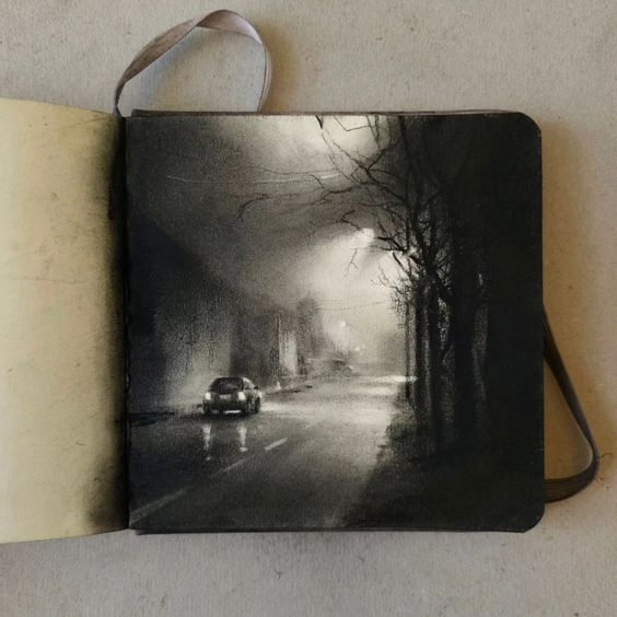 the image shows a charcoal or graphite drawing in a sketchbook. the drawing depicts a nighttime street scene, possibly in a city or suburban area.  the scene is rendered in a monochromatic palette of dark grays and blacks, creating a moody and atmospheric effect. fog or mist obscures the background, contributing to a sense of depth. the central focus is a single car driving down a street lined with trees.  streetlights are visible in the distance. the sketchbook is slightly open, revealing a tancolored page. a dark brown leather strap or binding secures the sketchbook.  the overall style is realistic and detailed, focusing on light and shadow to build form and atmosphere.
