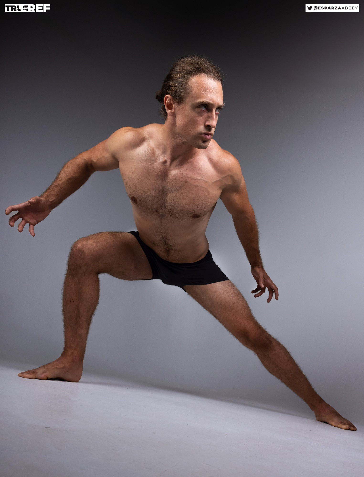 the image is a studio shot of a muscular male model in a dynamic pose. he's shirtless, wearing darkcolored underwear, and his body is positioned in a low, athletic stance, suggesting movement or action. the background is a neutral grey, and the lighting focuses on the model's physique. the overall style is suggestive of a reference image for artists or figure drawing studies, as it emphasizes anatomical detail and form.