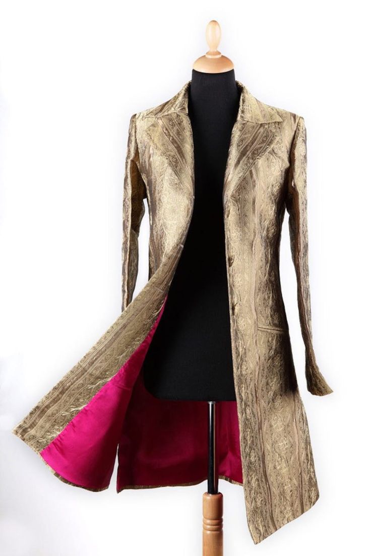 a gold, silk, long, vintage, coat, worn by a mannequin. the coat has a collar, long sleeves, lapels, buttons, and a pink lining. the fabric is textured with a rich, golden pattern.