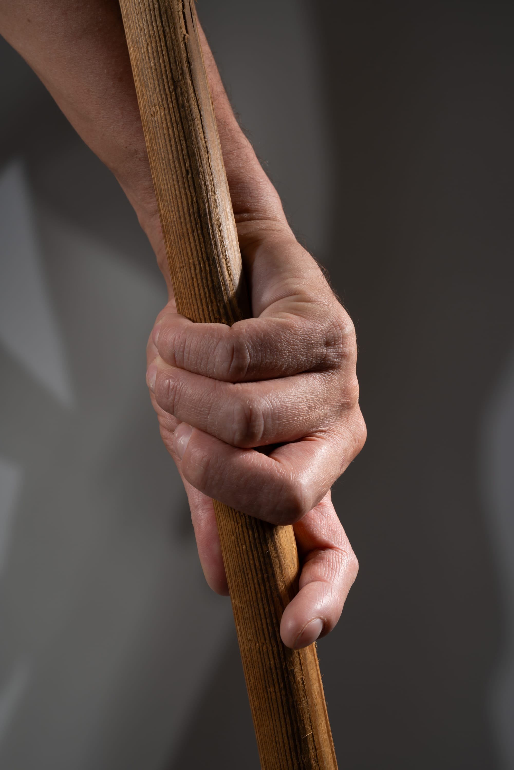 a closeup image of a man's hand tightly gripping a wooden stick. the hand is weathered and strong, conveying a sense of experience and resilience. the wood of the stick is worn and textured, adding to the rustic and natural feel of the image. the lighting is soft and directional, highlighting the details of the hand and stick.