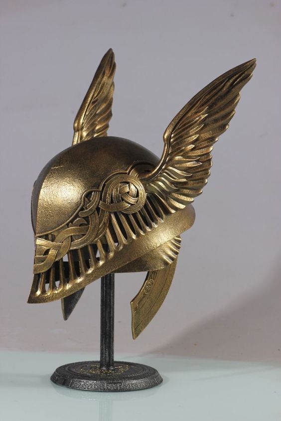 the image showcases a meticulously crafted replica of a winged helmet, likely inspired by valkyrie or goddess imagery from norse mythology or similar fantasy contexts. the helmet is predominantly goldcolored, with an intricate design featuring detailed winglike protrusions on either side and celticstyle knotwork patterns incorporated into its structure. the helmet rests on a darkcolored display stand, enhancing its presentation. the overall aesthetic is one of refined craftsmanship and detailed artistry, suggesting it could be a highquality collectible or decorative piece. the smooth lighting and neutral background emphasize the object's details. the helmet appears to be made of metal or a highquality metallike material.
