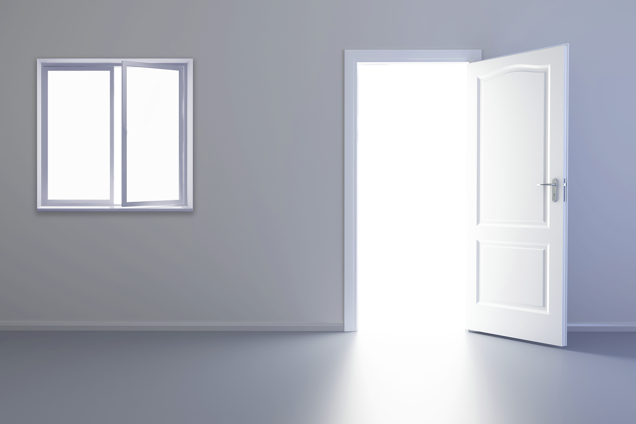 a room with a window and an open door. the window is a sliding window and is partially open. the door is white and open into a black space. the walls are gray and the floor is gray. there is light coming through the door and the window.