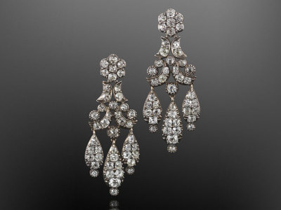 a pair of antique silver chandelier earrings with intricate designs and numerous diamonds are displayed against a dark gray background. the earrings dangle with multiple teardrop shapes and floral motifs, showcasing their sparkle and elegance.