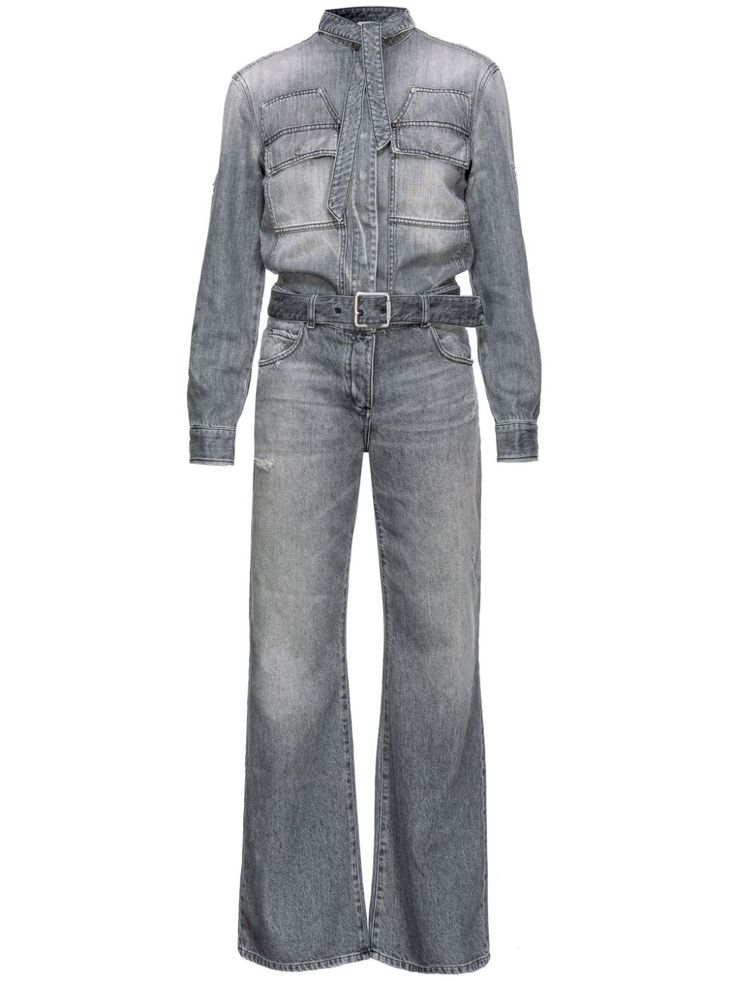 this is a photo of a woman wearing a gray denim jumpsuit with a belt. she is wearing a longsleeved button up shirt with two pockets on each side. the bottom of the jumpsuit is a wide leg silhouette and is fitted at the waist.