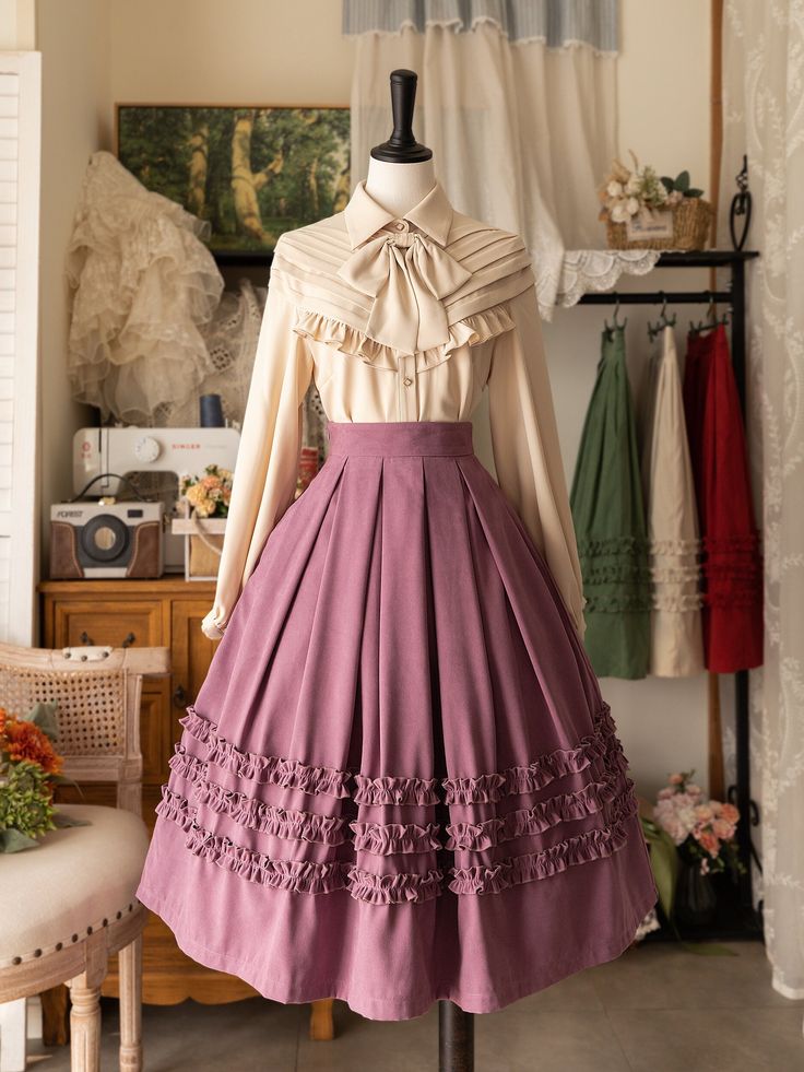 a vintageinspired dress is displayed on a mannequin. the dress features a flowing purple skirt with ruffled tiers and a creamcolored blouse with a bow. the background reveals a studio setting with hints of vintage furniture and decor.