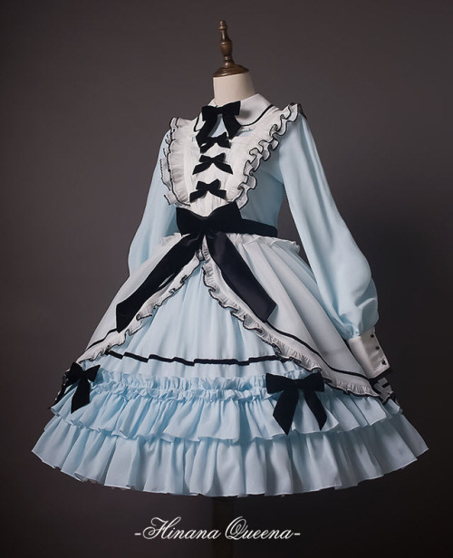 a light blue lolita dress on a mannequin. the dress features a white peter pan collar with black ribbon details, long sleeves with ruffled cuffs, and a tiered skirt with black ribbon accents. the skirt is full and fluffy, creating a voluminous silhouette.  the dress is set against a plain gray backdrop, highlighting its intricate details.