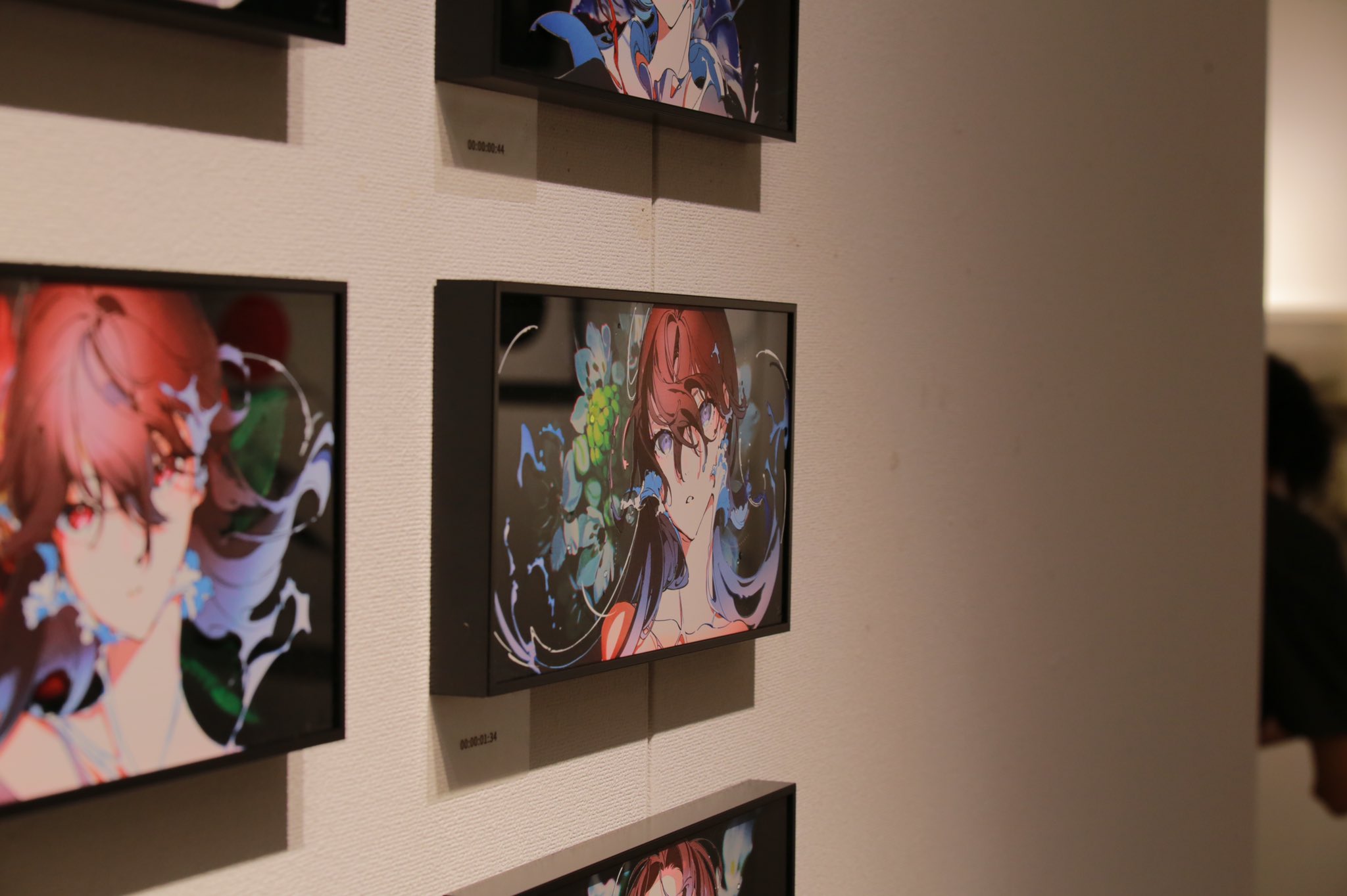 an art gallery wall with several framed digital paintings of an animestyle female character with flowing red hair. the frames are black and mounted to a white wall. the paintings feature a vibrant color scheme of blue, pink, and purple, contrasting with the neutral tones of the gallery setting. the image is taken at eye level, providing a direct view of the artwork and creating a sense of immersion in the exhibition space. the presence of a person in the background adds to the atmosphere of an art exhibition.