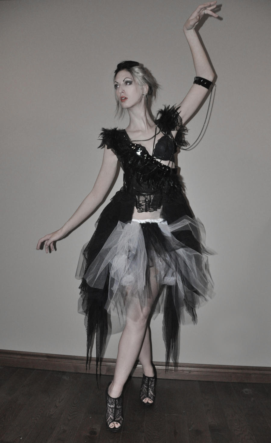 a full shot of a female model posing in a dramatic, darkthemed outfit. she is wearing a black and white tutu dress with a lace corsetstyle top. the dress features a black tulle overlay and a white tulle underskirt.  she has pale makeup and her hair is styled up. the background is a simple, lightcolored wall. her pose is artistic and expressive, with one arm elegantly raised. the overall tone is dark and moody, creating a striking and stylish image. she is wearing dark heeled shoes with lace detailing. the photo seems professionally taken in a studio.