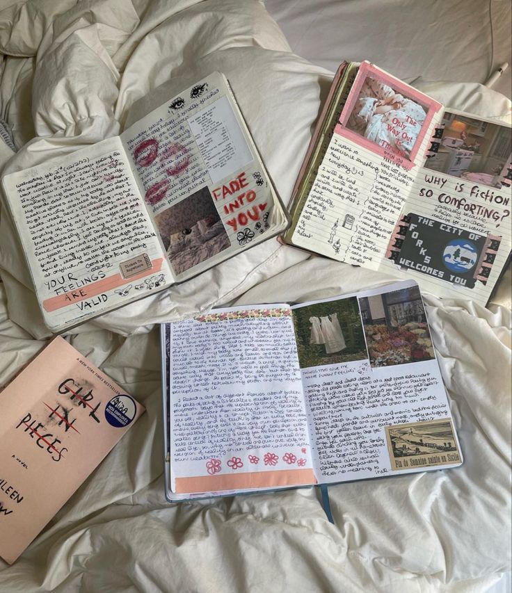an image showing an aesthetic flat lay of multiple journals with a book title "girl in pieces" on a bed with a white bedspread. all the journals are open on the page with handwritten text and pink flower decorations on them, the text in one of the journals is "fade into you", "the only way out", "why is fiction so comforting?", "the city of forks welcomes you".
