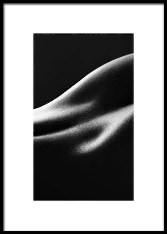 the image is a black and white closeup photograph of a human body, specifically focusing on the curves and texture of the skin. the lighting is dramatic, creating strong shadows and highlights that emphasize the form and contours of the body. the overall aesthetic is minimalist and sensual, with a focus on the abstract beauty of the human form.  the background is a deep black, drawing all attention to the softly lit curves of the body. the image is presented within a simple, black frame.