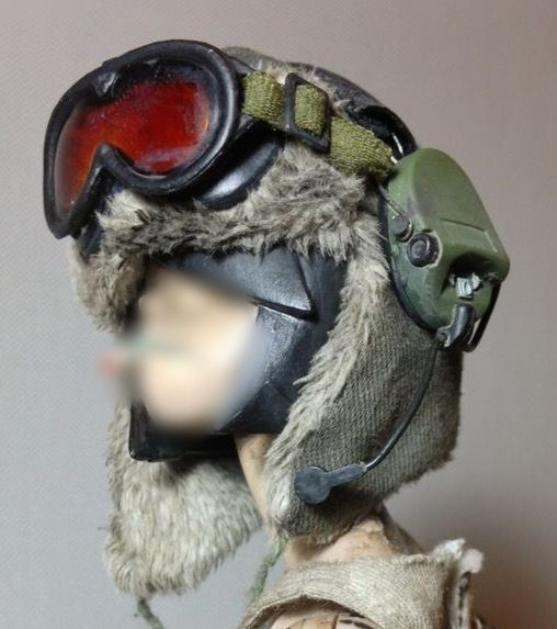 this is a closeup photo of a person wearing a winter hat with fur earmuffs,  goggles, and a camouflage face mask.