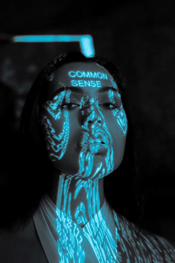 a closeup portrait of a young woman with long dark hair. her face is illuminated with a blue light that creates a digital, futuristic effect. the words "common sense" are projected onto her forehead. the image is dark, mysterious, and thoughtprovoking. it could be interpreted as a comment on the role of technology in our lives or the importance of common sense in a digital world.