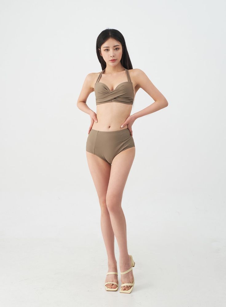 a fulllength studio shot of a slender young woman with long black hair, wearing a taupecolored highwaisted bikini. she is posing confidently, hands on hips, against a white background. she is wearing creamcolored heeled sandals. the image is welllit and focuses on the model's body and the swimwear.