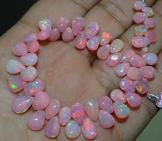 a closeup shot of a strand of pink opal teardrop beads. the beads are all different shades of pink and have a beautiful iridescent shine. the beads are arranged in a necklace pattern and are being held by a hand.