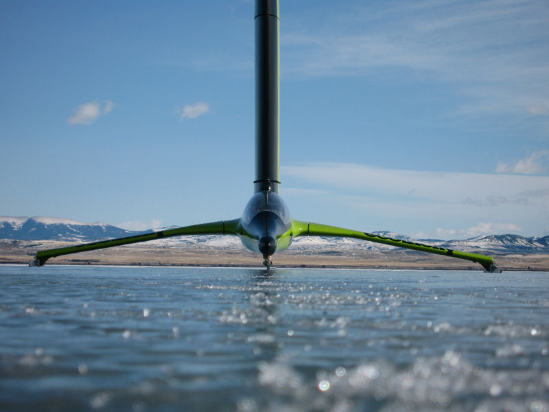 a green and black plane sits on a frozen lake with the mountains and blue sky behind it.