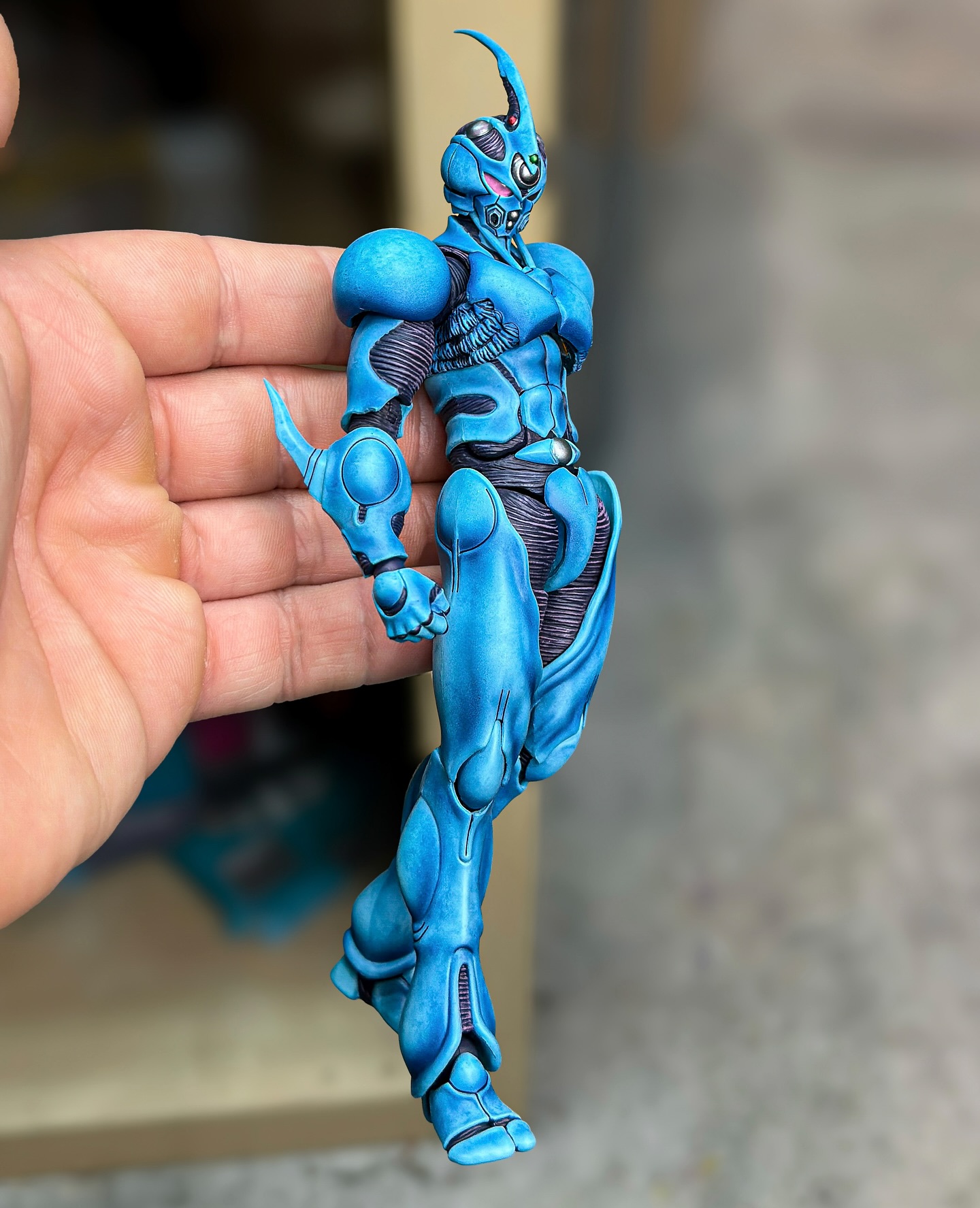 a detailed blue guyver action figure is being held in a person's hand.