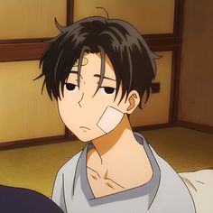 this is a close up illustration of an animestyle male character with short dark hair and bandages on his forehead and cheek. he has a tired or apathetic expression, and is wearing a light blue vneck shirt. he appears to be sitting on a bed in a room with light wood paneling. the overall lighting is soft, giving the image a slightly melancholic mood.
