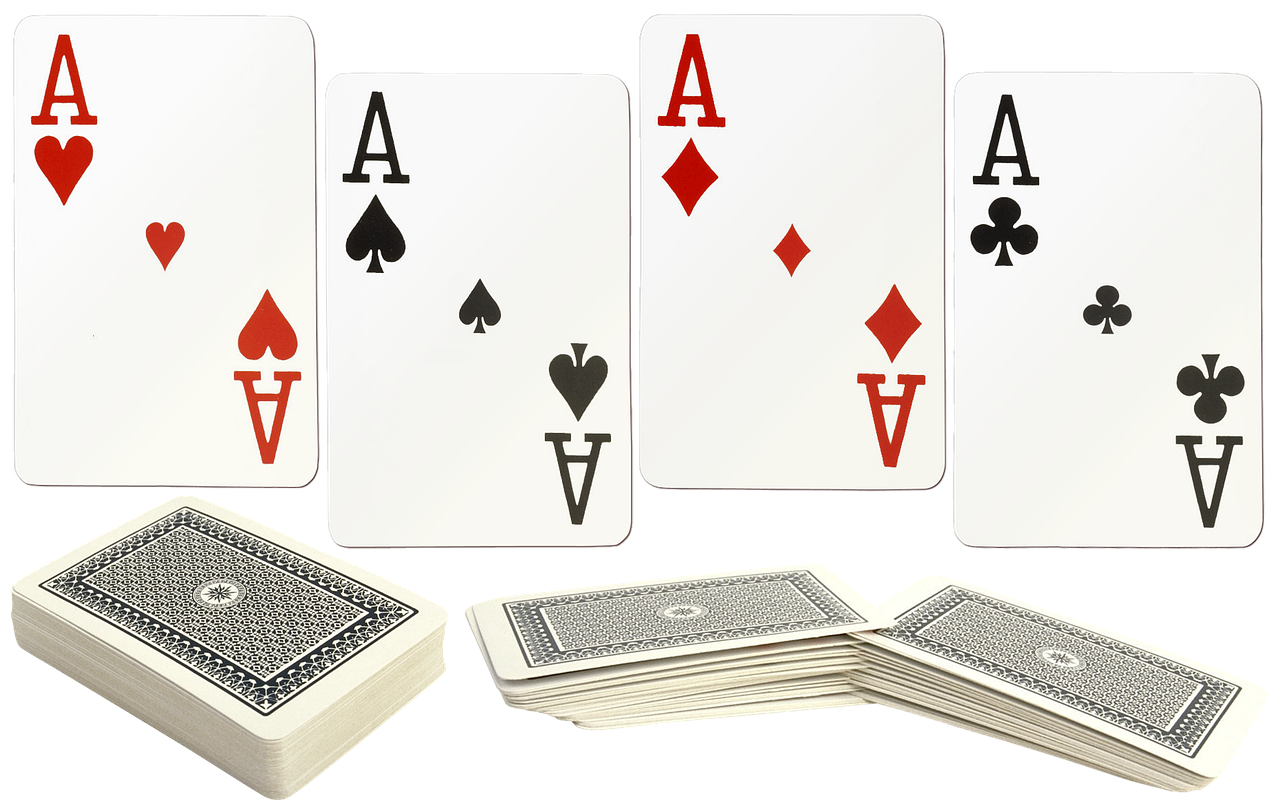 the image shows a full set of ace playing cards (hearts, spades, diamonds, and clubs) spread out above a pile of card decks with black and white patterned backs, set against a black background.