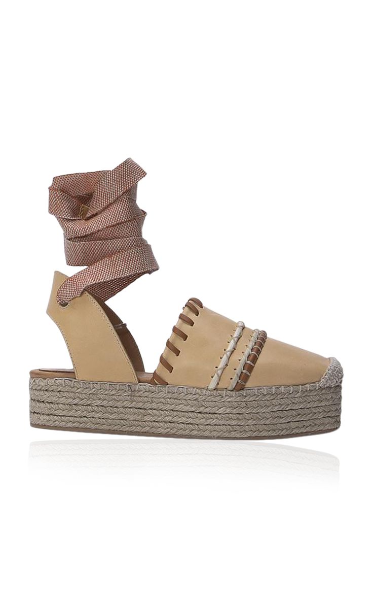 a closeup studio shot of a beige women's espadrille platform sandal with laceup ankle ties. the sandal has a woven jute platform and a beige leather upper with brown braided details. the overall aesthetic is summery and fashionable. the image is welllit and the background is white, allowing the shoe to be the focus.