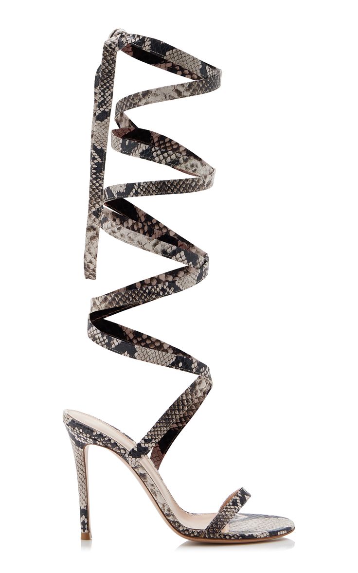 a pair of elegant highheeled sandals are shown in the image. the sandals are made of snakeskin material in beige, brown, and black colors. the straps of the sandals are wrapped around the ankle and leg multiple times, creating a unique and stylish look. the heels are stiletto style, adding to the elegance of the shoes.  the background is pure white, making the shoes stand out clearly.