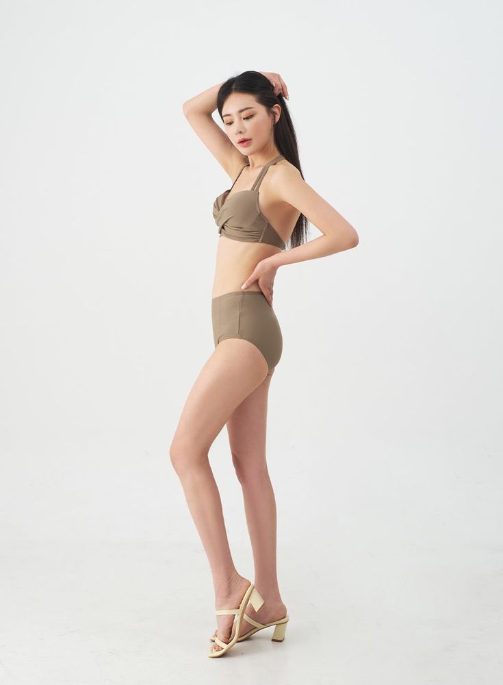 a full shot of a young asian woman in a taupecolored highwaisted bikini. she is standing with one hand on her hip, looking down. she is wearing light beige highheeled sandals. the background is plain white.