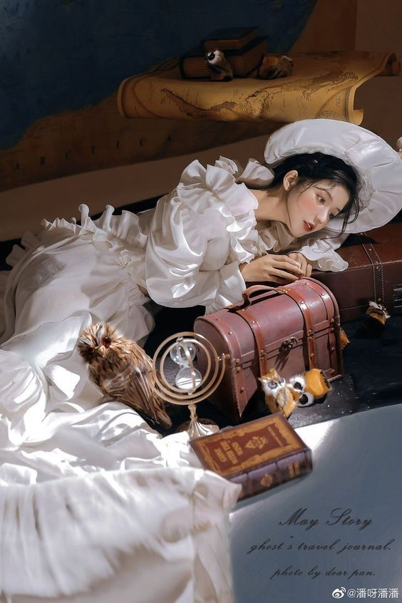 a woman in a white dress is lying on the floor next to a treasure chest, an owl, a globe, and a book. the room is decorated with a vintage map. the image has a soft and dreamy atmosphere.