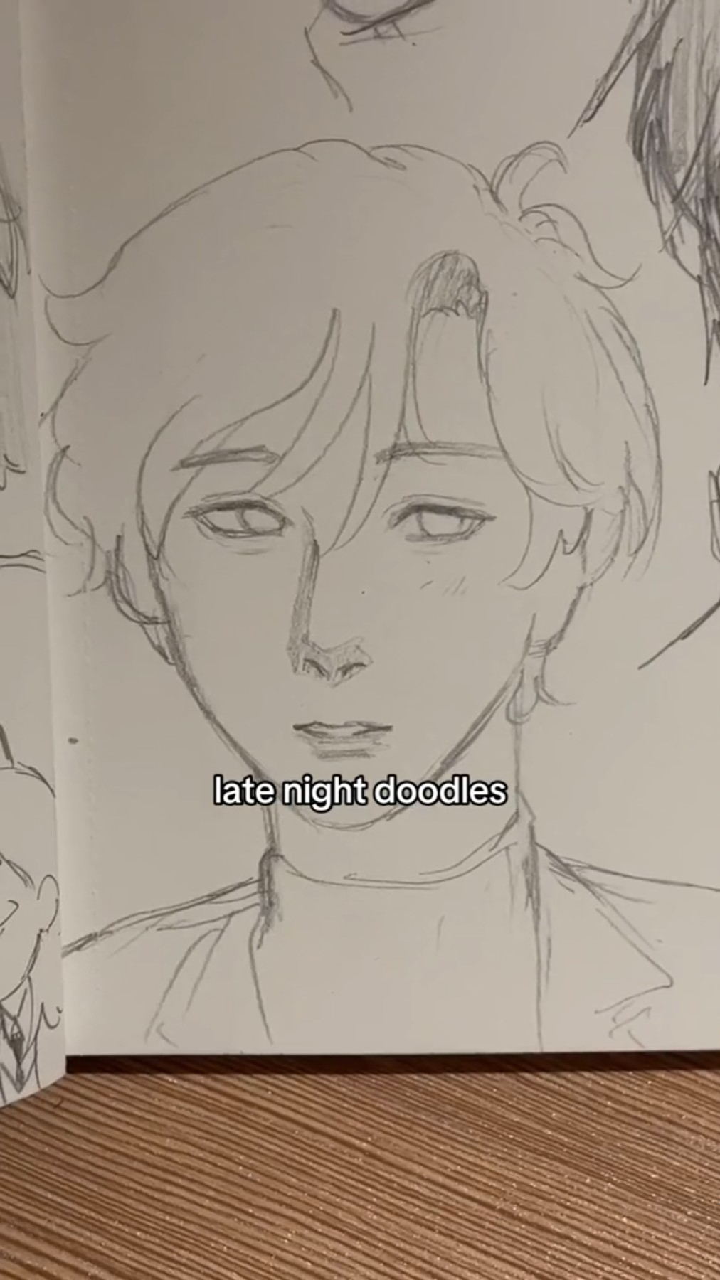 the image shows a page from a sketchbook with several unfinished pencil sketches of faces. one face, drawn with more detail and in the foreground, is that of a young man with mediumlength hair and a neutral expression. this drawing is labeled "late night doodles". the sketches are drawn in graphite pencil on white paper.  the lighting appears to be from above.