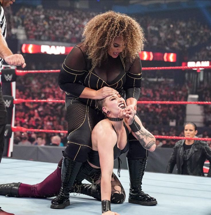 two female wrestlers are in the middle of a match. the wrestler on the top is in a submission hold, while the wrestler on the bottom is trying to break free. there are other wrestlers in the background, and the crowd is cheering.