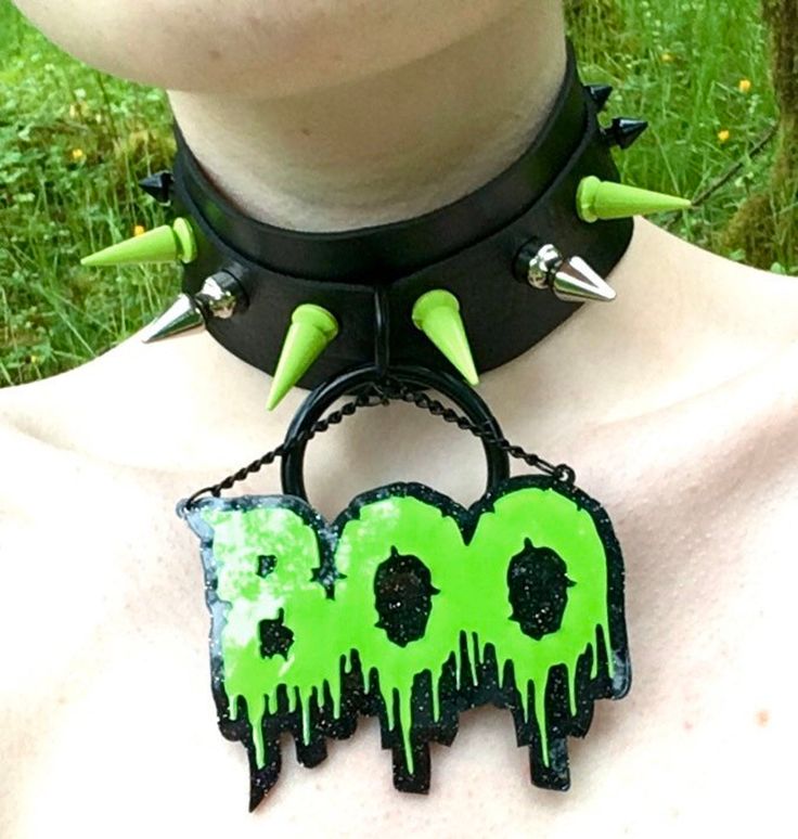 this image shows a person wearing a black choker with green spikes. the choker is attached to a green and black pendant that says "boo." the person is also wearing a black shirt. the image appears to be a style for goth or punk fashion and is likely for halloween.