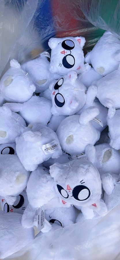a large pile of white plush toys with cute cat faces. they are all soft and fluffy and have big, black eyes. the toys are arranged in a haphazard pile, with some of them peeking out from behind others. the image is full of cuteness and makes you want to reach out and touch the toys.