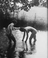 a black and white photograph depicting two nude women bathing in a shallow river. the women are standing in the water, their bodies partially submerged. the background is a natural landscape with trees and foliage. the overall mood is serene and peaceful. the photograph has a vintage or historical feel.