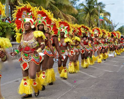 a vibrant street scene captured during a carnival parade in the caribbean. the image shows a group of dancers in colorful costumes and headdresses, moving rhythmically through the streets. the dancers are adorned with feathers, sequins, and vibrant fabrics, showcasing the richness and energy of caribbean culture. the scene is full of life and joy, capturing the essence of the carnival celebration.