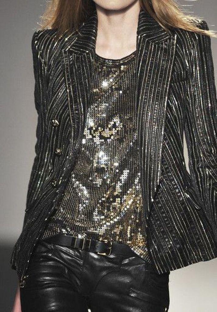 a woman in a black and silver striped blazer with gold accents, a silver sequin top and black leather pants.  she has a stylish look.