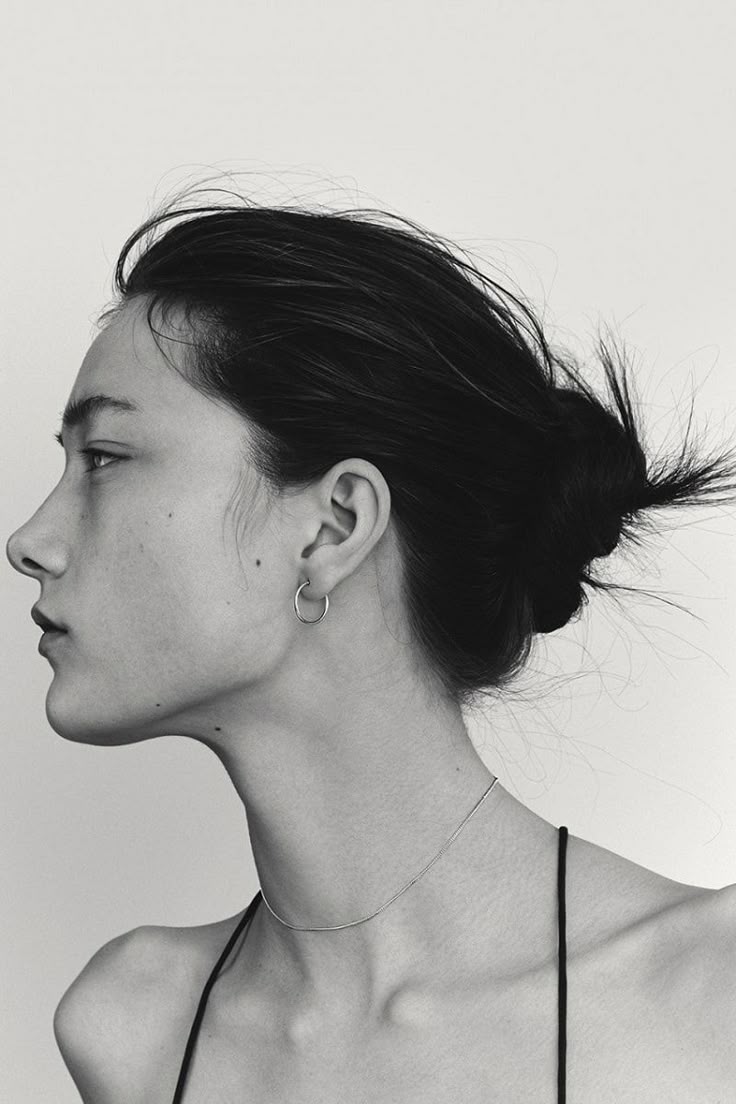 a black and white profile portrait of a woman with her hair in a bun, wearing hoop earrings and a thin necklace.