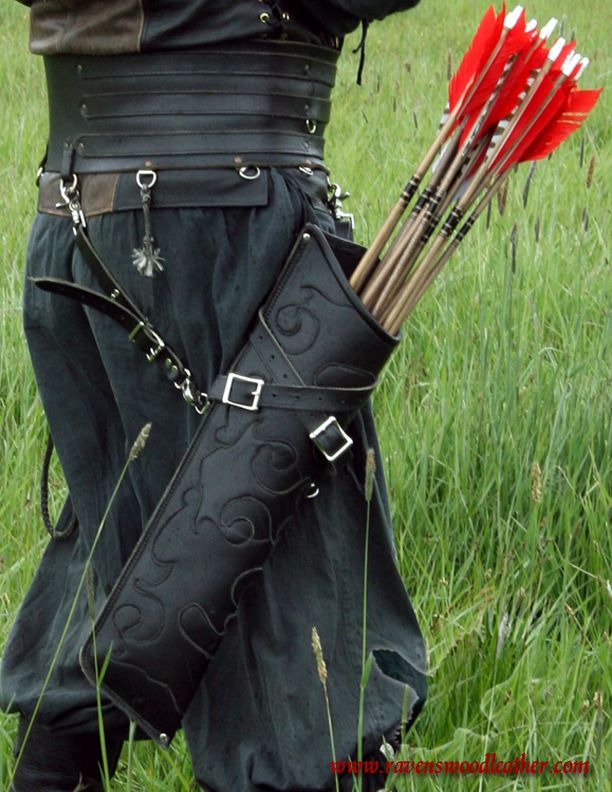 a person wearing medieval or renaissance style garb with a leather quiver full of arrows attached to their belt. the arrows have red feathers. the person is standing in a grassy field.