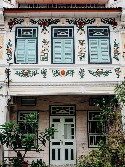 a meticulously preserved shophouse in singapore stands as a testament to the country's rich architectural heritage. the building's facade, adorned with intricate floral motifs and pastel hues, showcases traditional design elements.  the light mint green window shutters and doors contrast beautifully with the white walls, creating a visually stunning composition. lush greenery surrounds the building, adding a touch of vibrancy and life to the urban scene.  the overall aesthetic is one of calm beauty and preserved history.