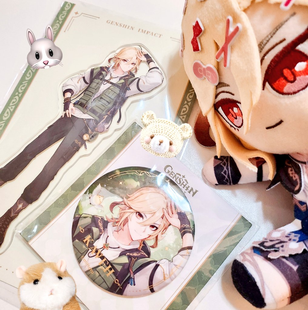 the image is a closeup of various genshin impact merchandise laid out on a table.  there is a large acrylic standee of kaeya, a small keychain of albedo, and a plush doll of a male character,  the image is bright and colorful, and the merchandise is all very high quality.