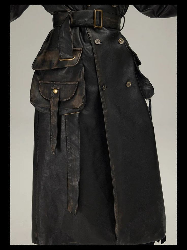 closeup view of a woman's black leather trench coat. the coat is long, doublebreasted, and features a large, distressed leather bag attached to the side.  the bag has additional pockets and is secured with straps and buckles.  the coat itself has a wide belt and flap pockets. the overall style is vintage or potentially gothic/steampunk inspired, with a distressed, worn look to the leather.  the image shows the coat from the front, focusing on the details of the coat and the attached bag.