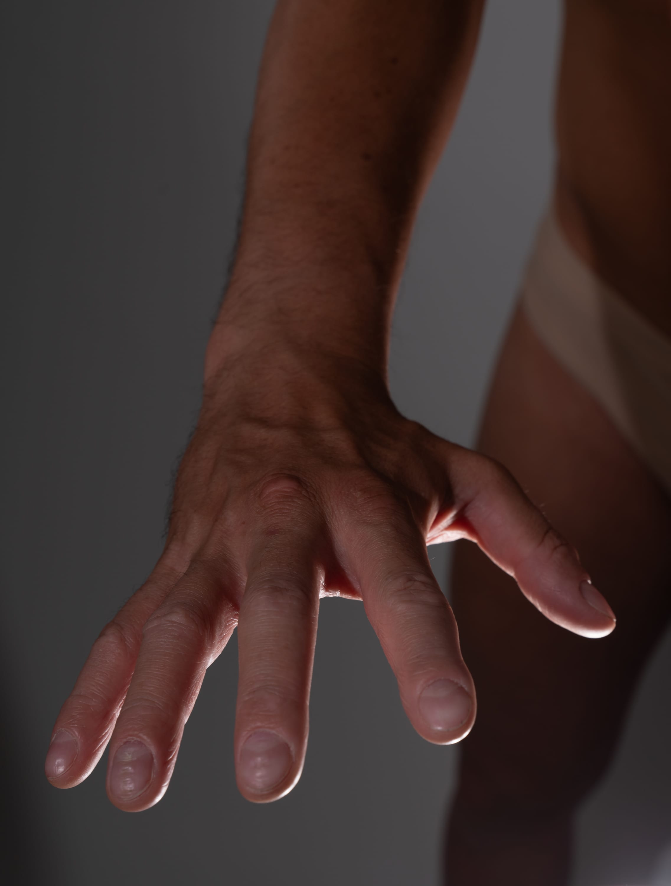 a closeup image of a man's outstretched hand and arm, illuminated by soft directional lighting. the focus is on the details of the hand, with the background and the rest of the body blurred.