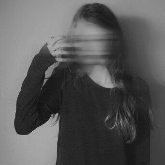 a woman is sitting in a studio with her face blurred, she is wearing a black sweater and has long hair covering her face, the image is in black and white.