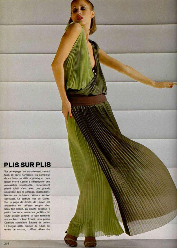a vintage magazine photograph of a woman wearing a green, pleated dress. she is posed in a flowing position with the wind blowing her dress. the model has a bright, youthful look with reddish brown hair and bright red lipstick. the photo is from a vintage magazine and has a vintage feel.