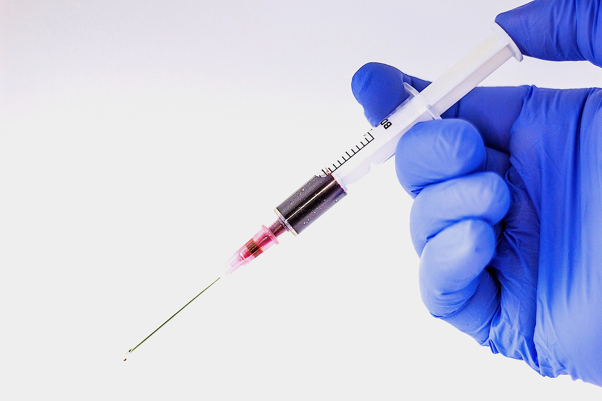 a gloved hand holds a syringe filled with a dark red liquid, likely blood or medication, poised for injection. the needle is clearly visible.