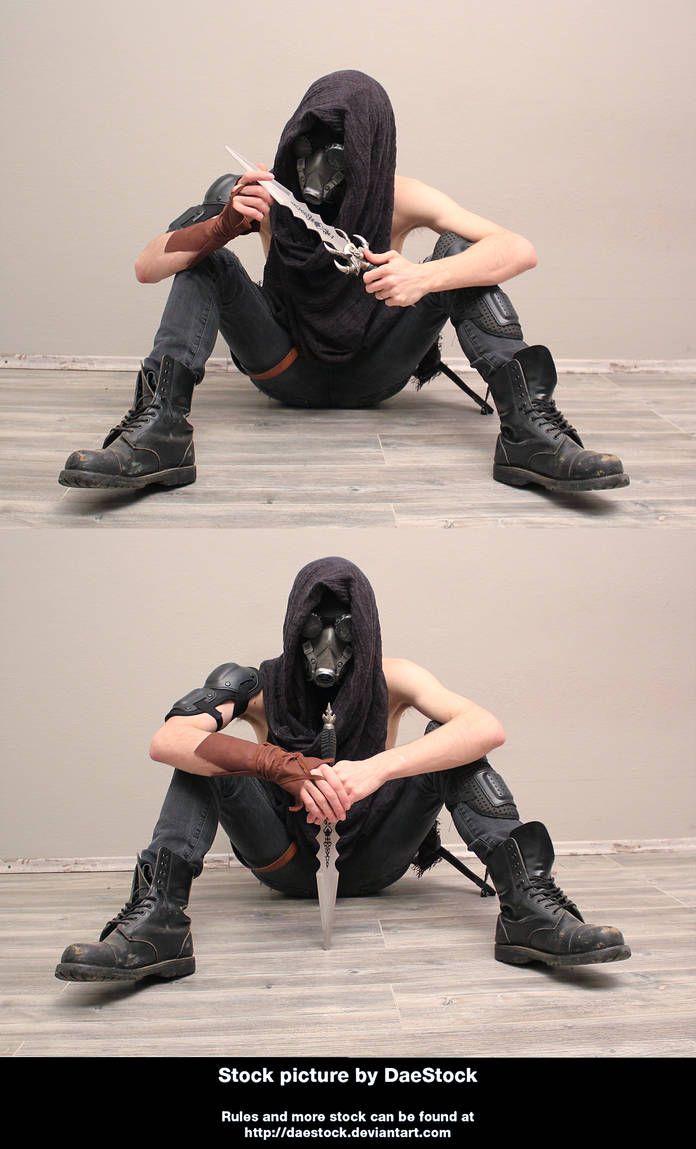 a man wearing a black cloak, mask, and combat boots sits on the floor with a dagger in his hand. he looks fierce and dangerous, as if ready for battle. the image is dark and mysterious.
